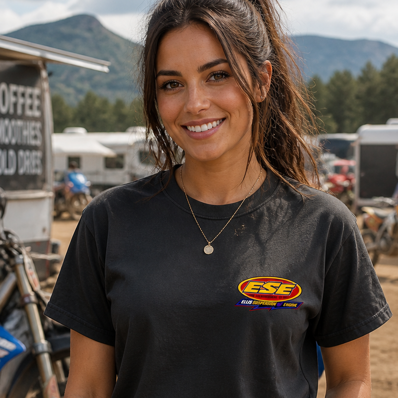 Woman wearing a black t-shirt with a logo at an outdoor event with motorcycles and trucks.